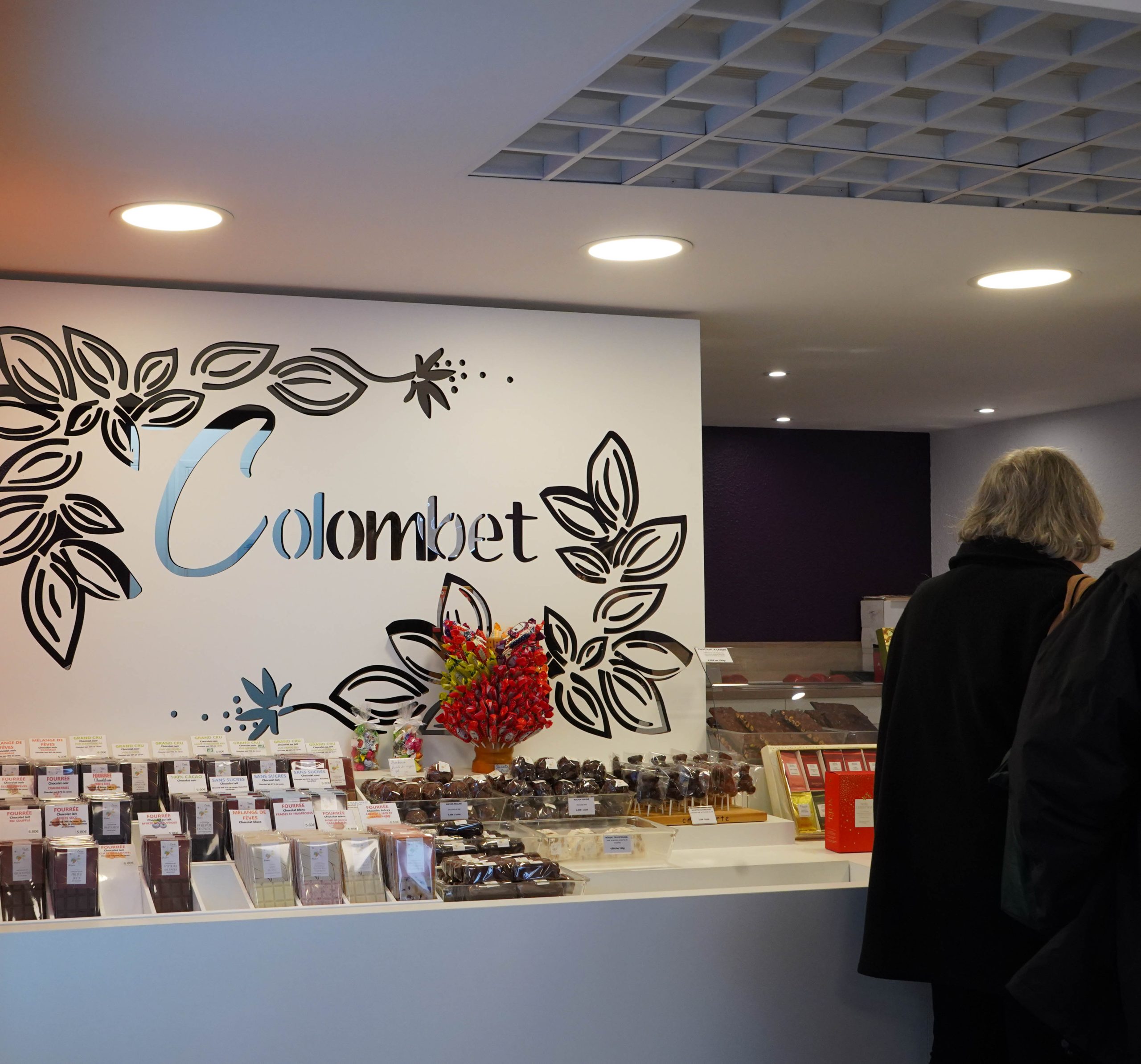 Comptoir de vente de la chocolaterie Colombet avec présentoirs de chocolats et mur décoré du logo, photographie réalisée dans le cadre des services de communication à Clermont-Ferrand, exemple de réalisation en communication 360° à Clermont par Clap Agency.